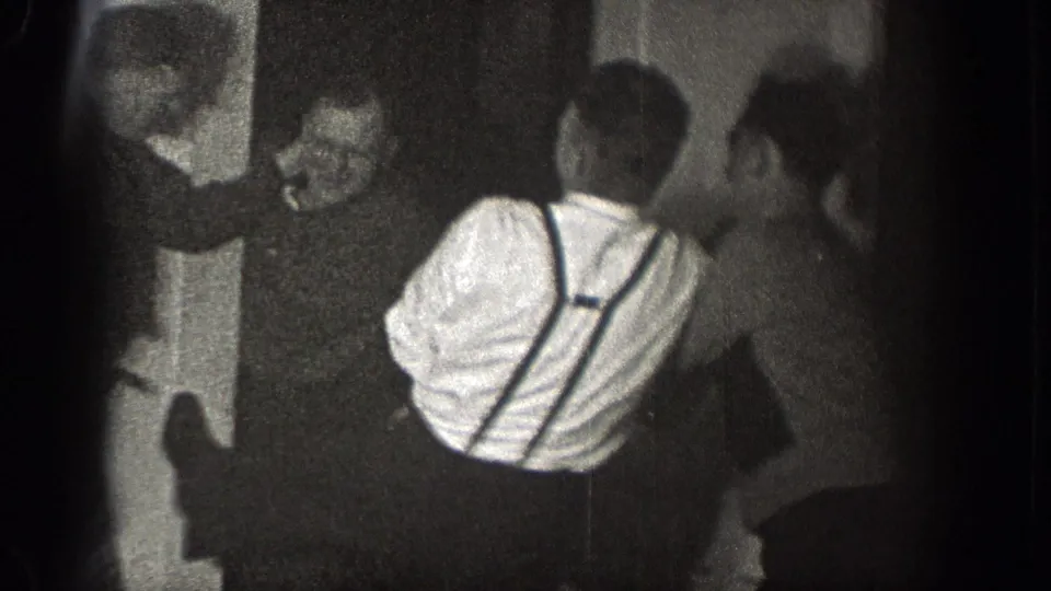 In a Chelan, Washington interior, several adult men appear to grapple near a door as the home-movie camera records from close range.