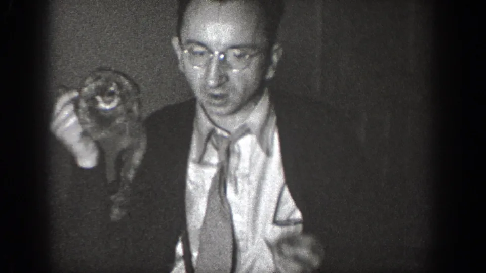 A suited man with glasses holds a small animal close to the camera in grainy 1939 Chelan home-movie footage.