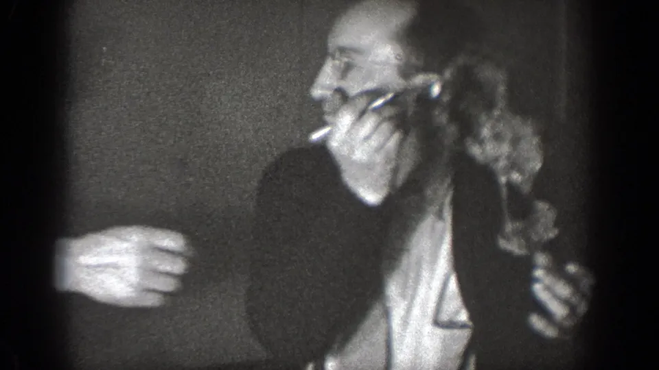 In a 1939 Chelan, Washington home-movie frame, suited adult men cluster tightly indoors during a tense table-side moment.