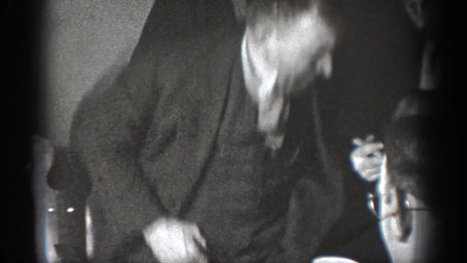 A suited adult man bends forward in a dim 1939 home-movie interior, with another cropped figure nearby.