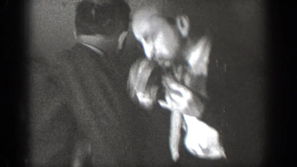 Near the end of the Chelan clip, adult men in suits remain closely grouped in a shadowed interior confrontation.