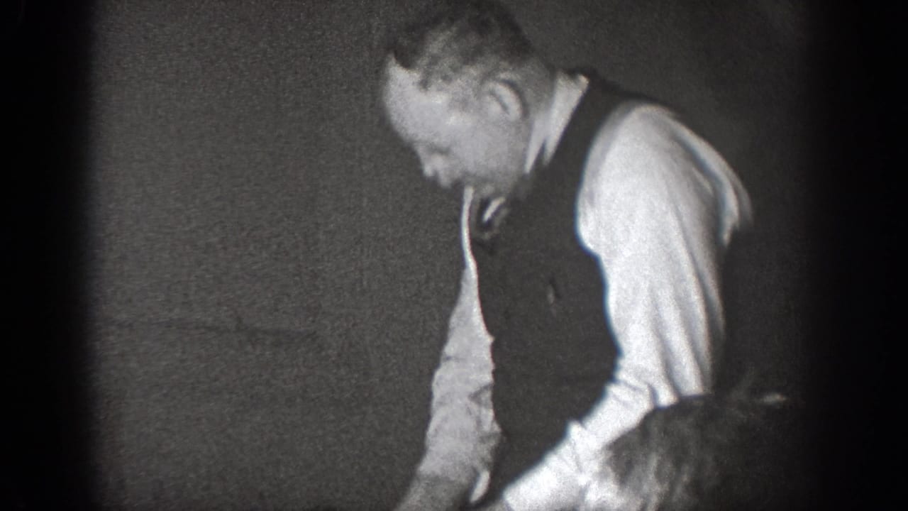 In a 1939 Chelan, Washington home-movie frame, a man in a vest and dress shirt appears to work over a table indoors.