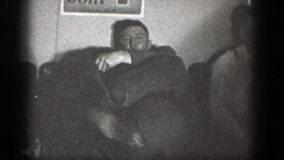 1939 Chelan, Washington home-movie frame showing adult men in a dim interior with upholstered seating and a framed wall picture.