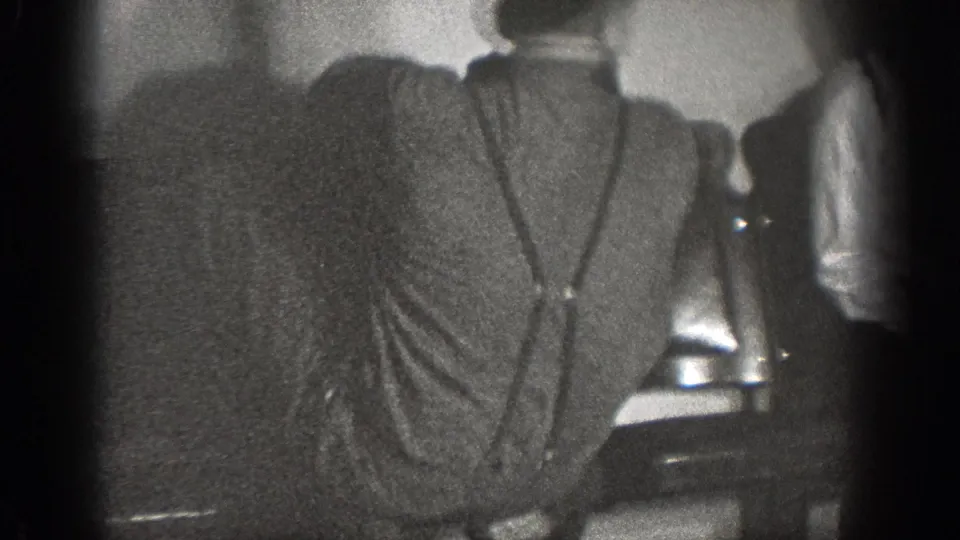 Chelan, Washington 1939 frame showing the back of a man in a grey shirt and suspenders inside a dim room.