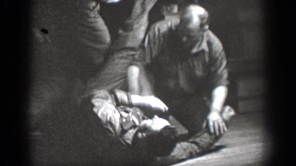 Near the end of the Chelan clip, two men are still on the wooden floor while another adult stands partly in frame.