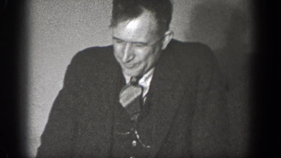 In 1939 Chelan home-movie footage, a man in a dark suit and tie smiles while seated close to the camera in a dim room.