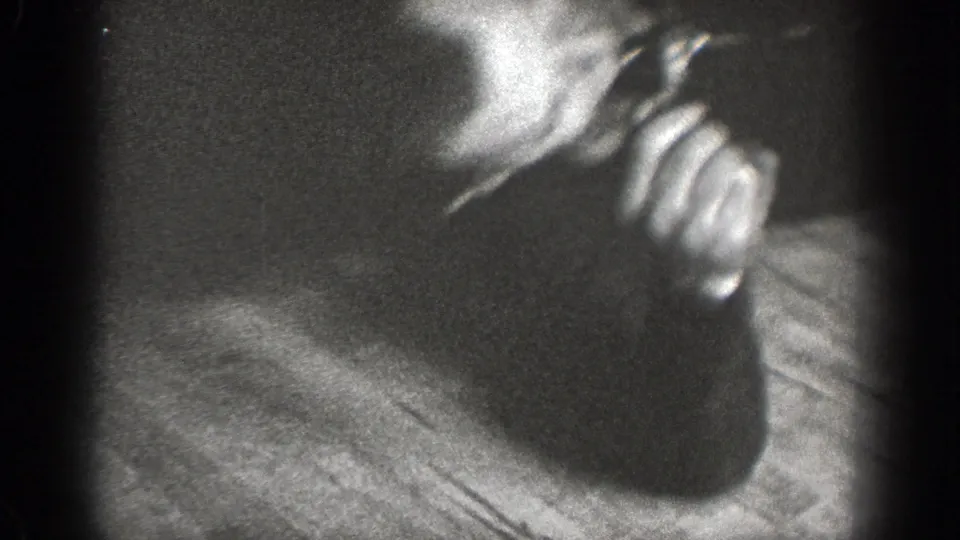 In 1939 Chelan home-movie footage, a man in a light shirt and tie bends close to another person in a dark, grainy indoor scene.