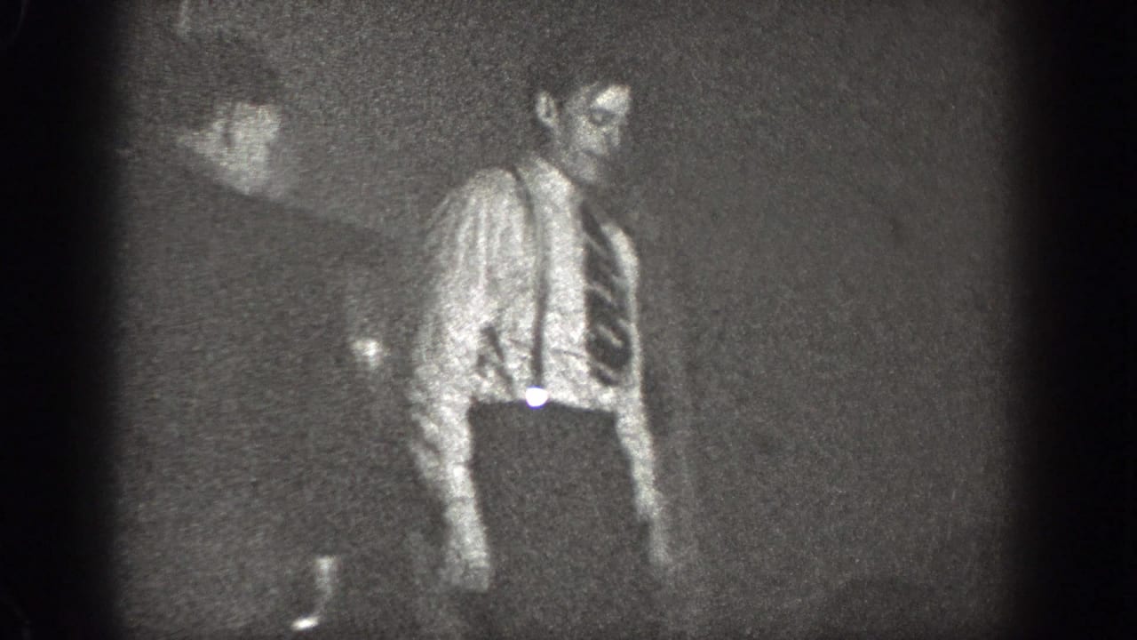 Man in shirt and tie stands in a dark interior with soft 8mm grain.