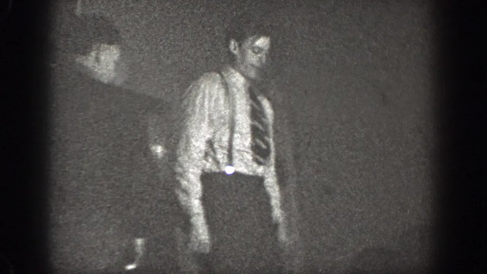 In 1939 Chelan home-movie footage, a man in a shirt and tie stands in a dim room as the frame falls into shadow.