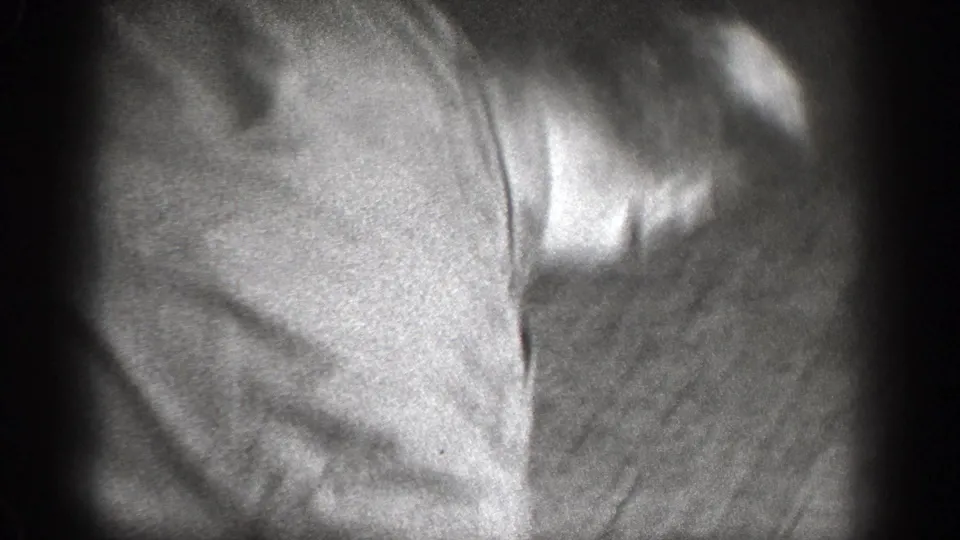 A blurred 8mm frame shows clothing and arms pressed close together as the indoor altercation continues.