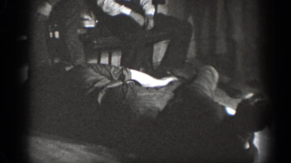 1939 Chelan home-movie frame showing bystanders seated and standing around a low indoor struggle.