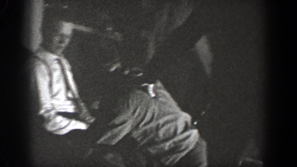 1939 Chelan frame showing men in a private interior with one figure low and others leaning nearby.