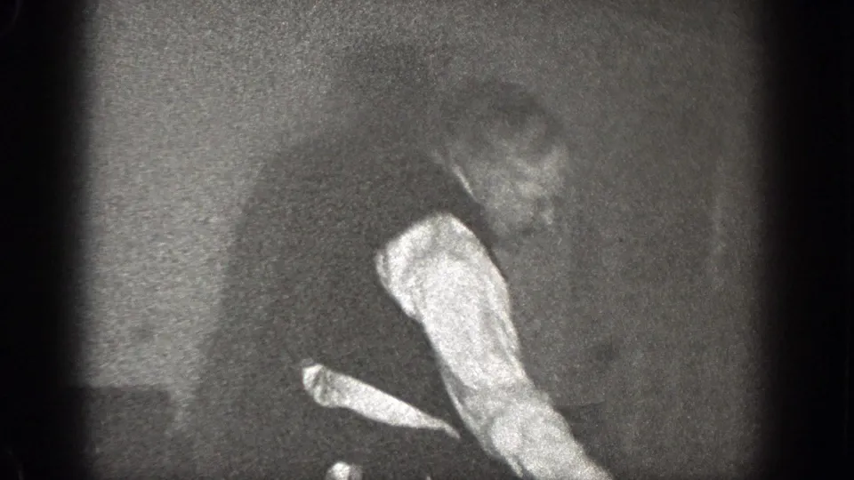 In a 1939 Chelan, Washington home-movie frame, a man in a vest and light shirt moves through a dark interior.