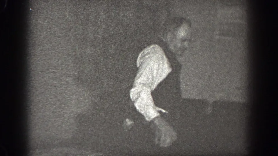 The man appears near a wall in the Chelan interior, with his light shirt standing out against the dark 8mm frame.