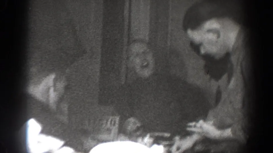 1939 Chelan home-movie frame showing adult men at a table in a dim private interior, with food and drinkware visible.