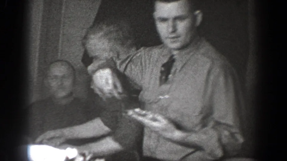 Adult man in a button-down shirt and tie appears to serve food in a 1939 Chelan indoor gathering scene.