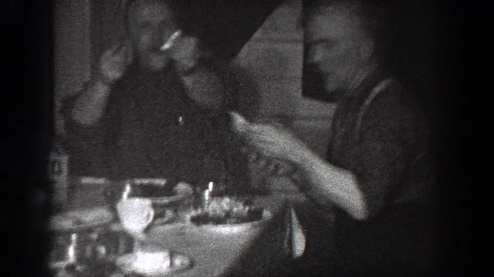 1939 Chelan frame showing men eating at a small table, one raising food or a utensil near his mouth.