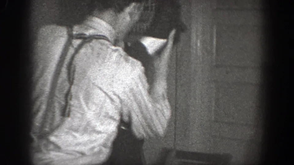 A person in a light shirt and suspenders is seen from behind near a wall or doorway in the Chelan interior footage.