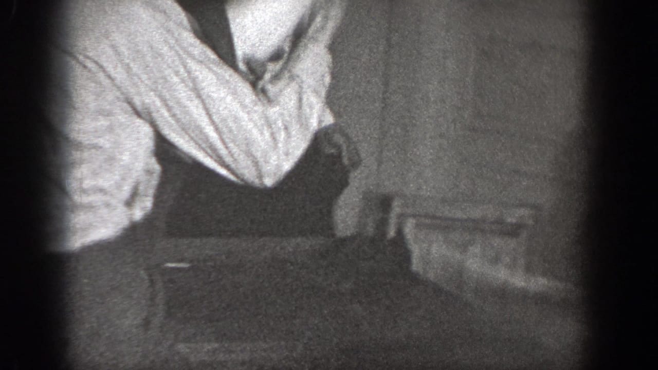 1939 Chelan home-movie frame showing a cropped adult man in a light shirt and suspenders inside a dim private room.