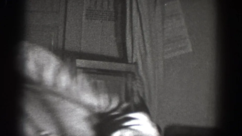 1939 Chelan home-movie frame showing men leaning during the joke, with interior furniture and a hanging garment behind them.
