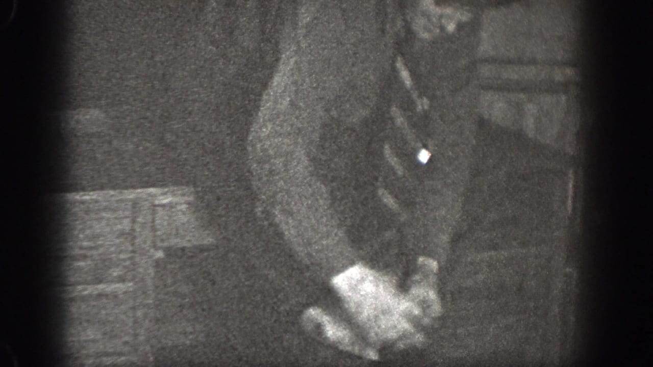 In 1939 Chelan, Washington footage, a man in a dark suit sits indoors with his hands near his lap in soft, grainy light.