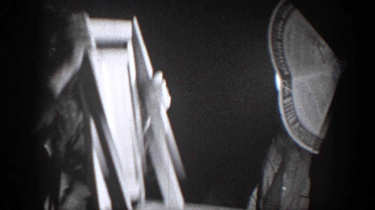 In the Chelan, Washington 1939 home-movie footage, a suited man raises or carries a wooden chair inside a dim room.