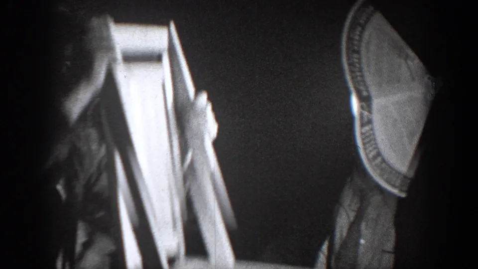 In the Chelan, Washington 1939 home-movie footage, a suited man raises or carries a wooden chair inside a dim room.
