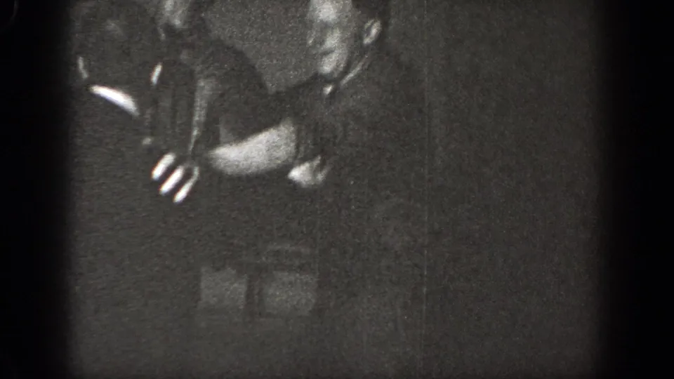 A man bends forward with outstretched arms as the brief indoor mock fight continues in the 1939 Chelan home movie.
