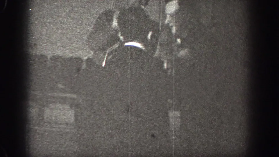 In Chelan, Washington 1939 home-movie footage, two adult men appear close together in a dim interior with heavy grain and soft focus.
