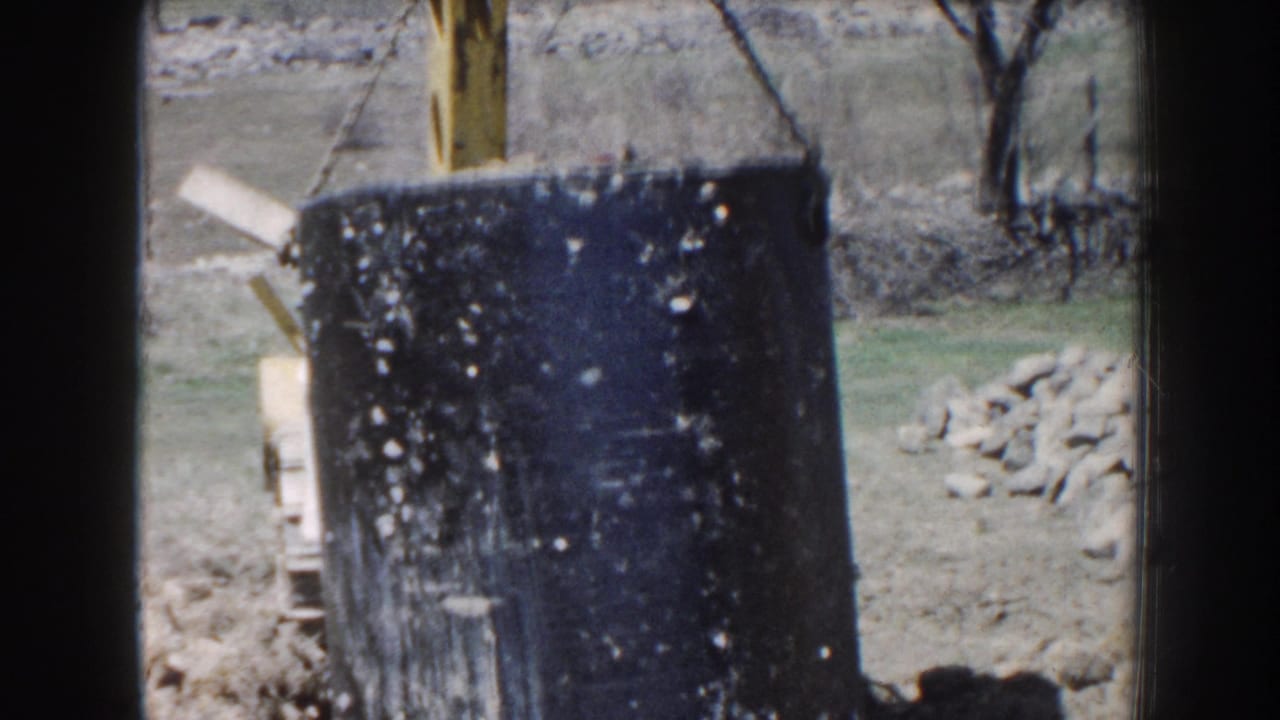 In Nebraska 1959 footage, a large black septic tank appears suspended near open ground, rocks, bare trees, and a trench.