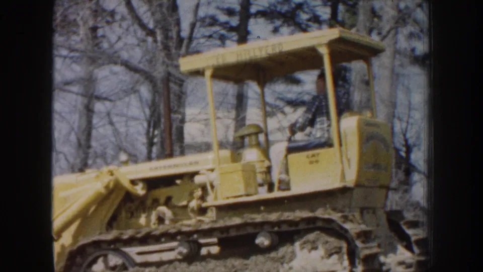 1959 Nebraska 8mm frame showing a side view of a yellow Caterpillar-style tracked bulldozer with an open canopy.