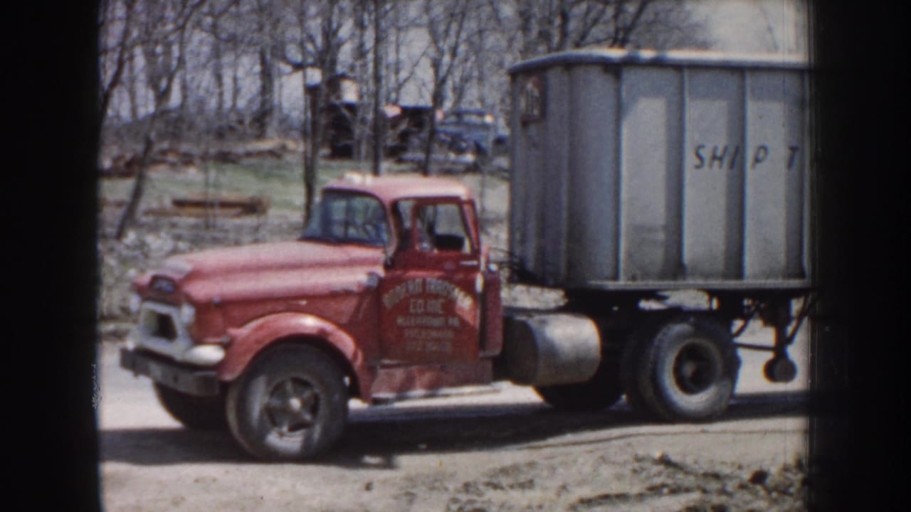 Red vintage truck beside a gray trailer on a roadside with bare trees behind it.