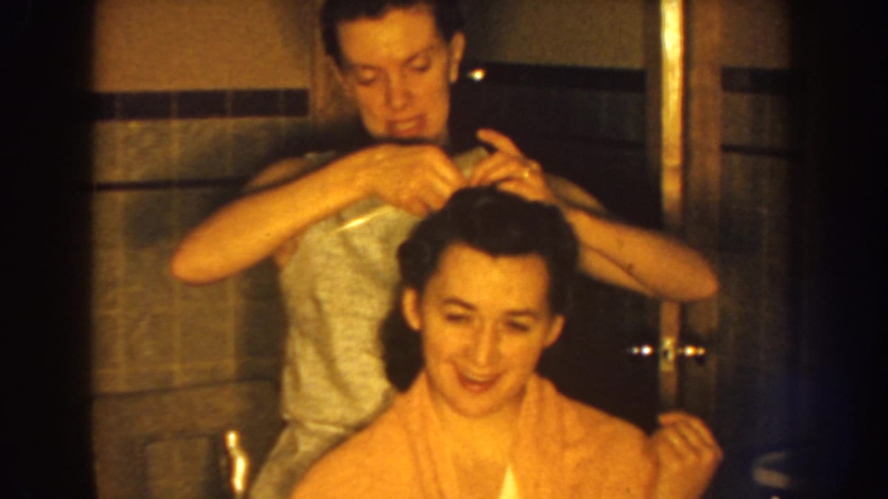 Young woman fixes another young woman's hair in a bathroom.