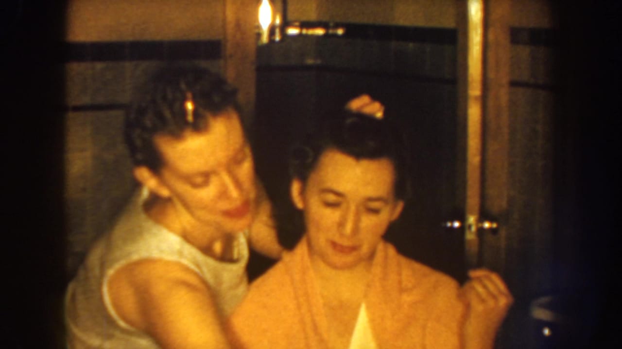 A young woman in a sleeveless top leans close to place or adjust a pin in another young woman's curled hair inside the Nebraska home bathroom.