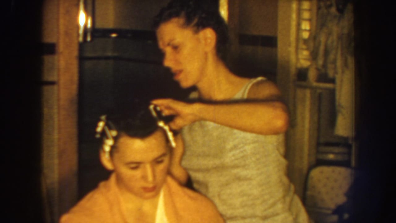 Woman adjusts the boy's hair while he sits with a towel around his shoulders.
