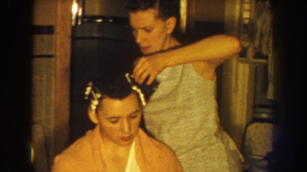 Woman arranging hair rollers on a seated woman's dark hair indoors.