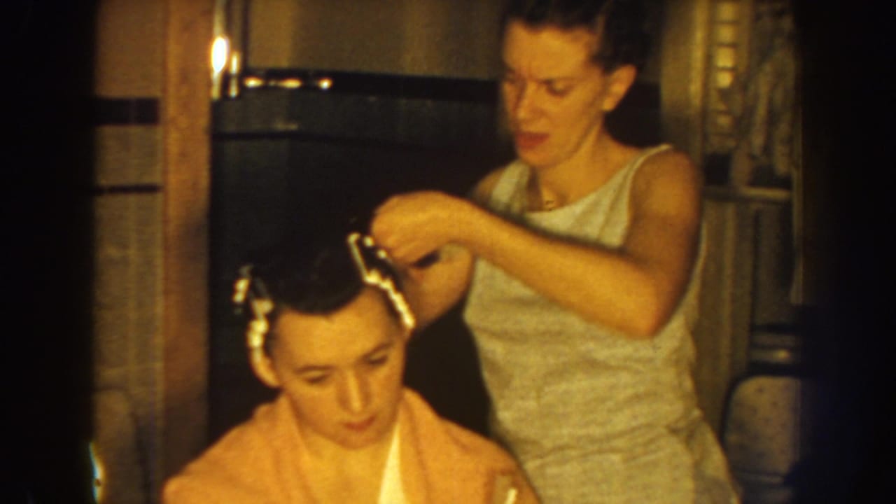 In this 1959 Nebraska home interior, a standing woman adjusts hair rollers while the seated woman faces downward.