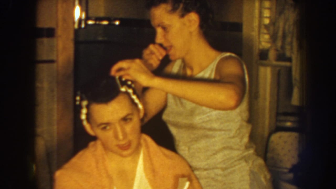 Woman sets curlers in a seated woman's hair inside a warmly lit room.
