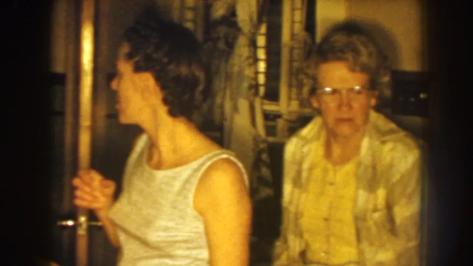 Inside the Nebraska home, the woman who was setting hair turns toward an older woman in glasses standing near the doorway.