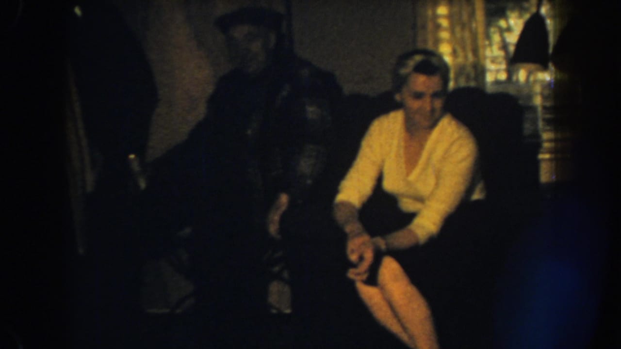 Woman seated with legs crossed looks to the side as a man remains behind her.