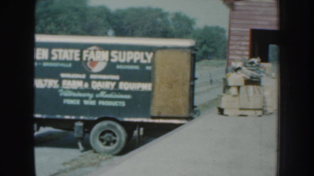 Farm supply truck beside stacked goods near a building entrance.