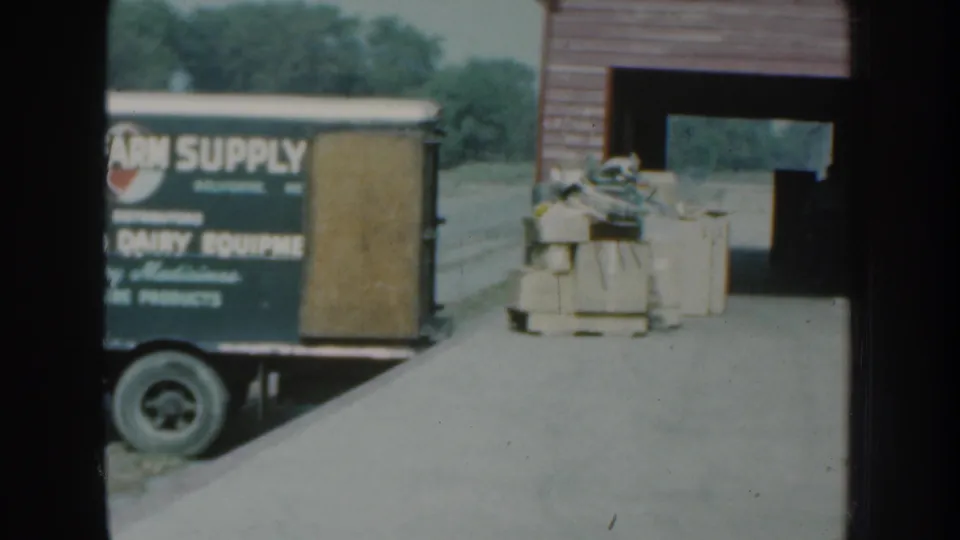 1959 Nebraska 8mm frame showing the rear portion of a farm supply truck and goods staged outside a rural building.