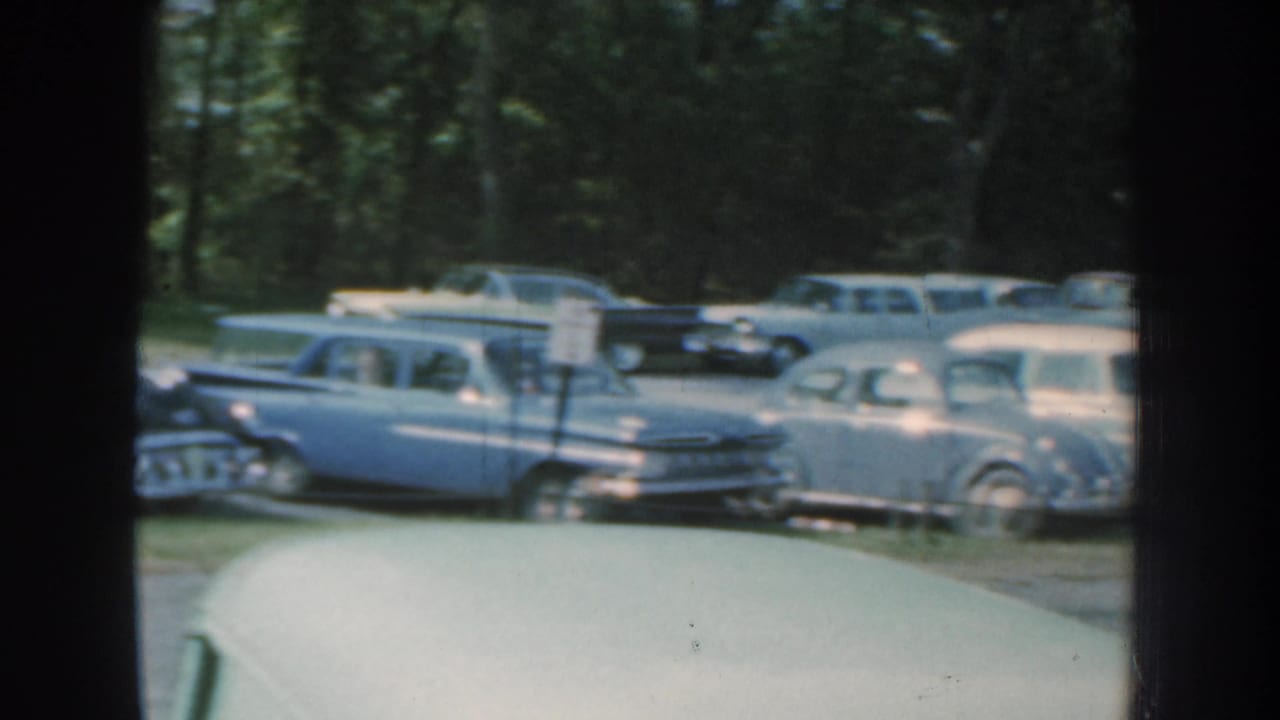 Classic cars parked on grass behind dark vertical window framing.