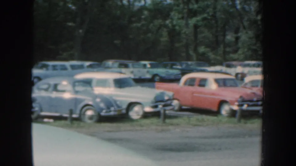 Nebraska 1959 frame with several late-1950s American cars, including pale sedans and a red-and-white wagon, parked near trees.