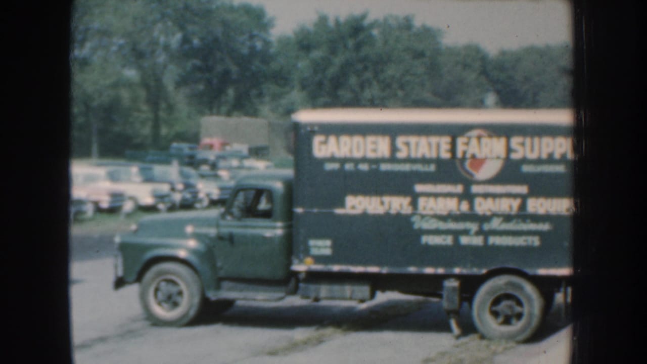 Green Garden State Farm Supply truck parked near classic cars in daylight.