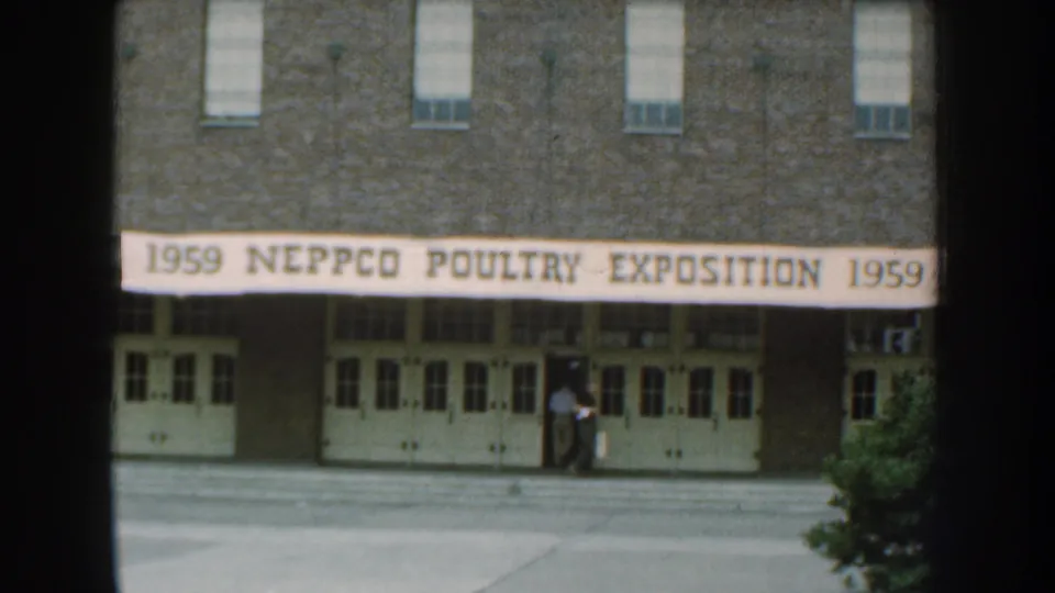 1959 Nebraska home-movie view of the NEPPCO Poultry Exposition banner on a brick hall, with visitors standing near the entrance.