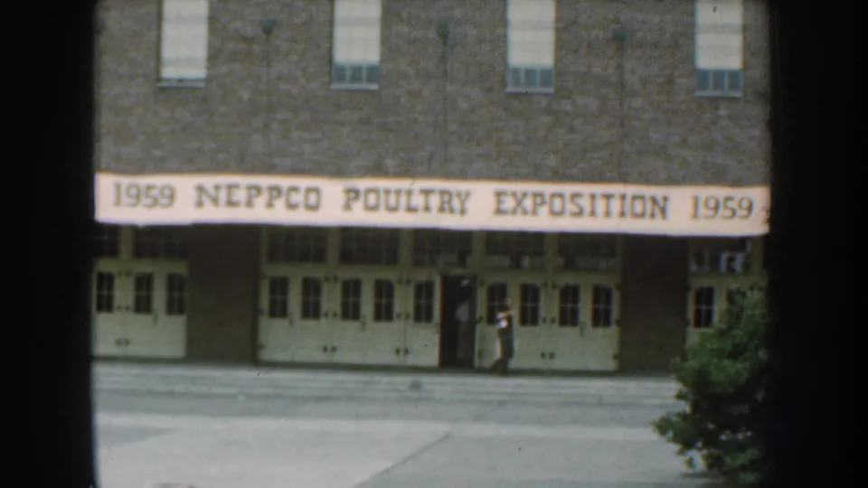 Nebraska 1959 8mm frame showing the NEPPCO Poultry Exposition banner across a brick building entrance with a person near the doors.