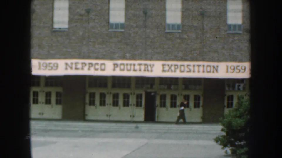 Nebraska 1959 8mm frame with the poultry exposition banner above white doors and a man passing in front of the entrance.