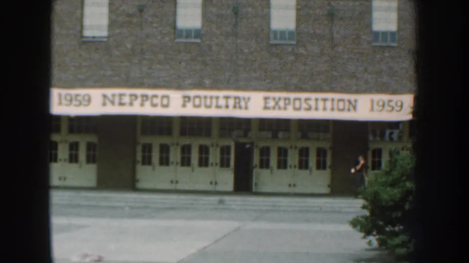 1959 Nebraska 8mm frame showing a brick building entrance and large NEPPCO Poultry Exposition banner across the facade.