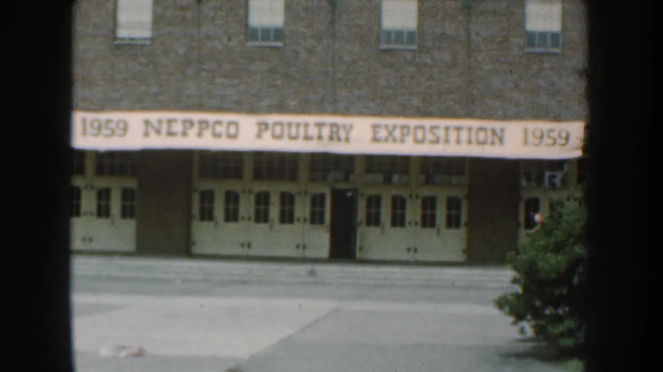 Home-movie frame of the 1959 NEPPCO Poultry Exposition sign on a Nebraska building, with soft grain and dark frame edges.